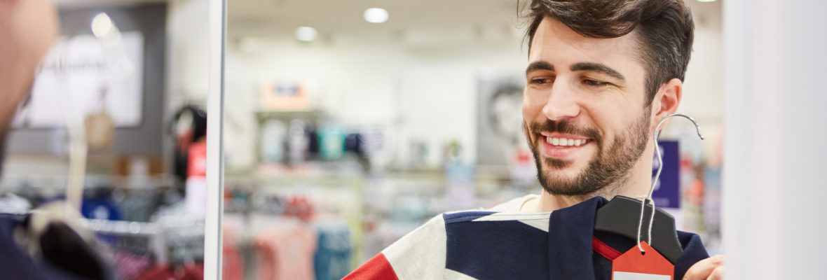 Junger Mann beim Shopping probiert ein Hemd im Einzelhandel Discount