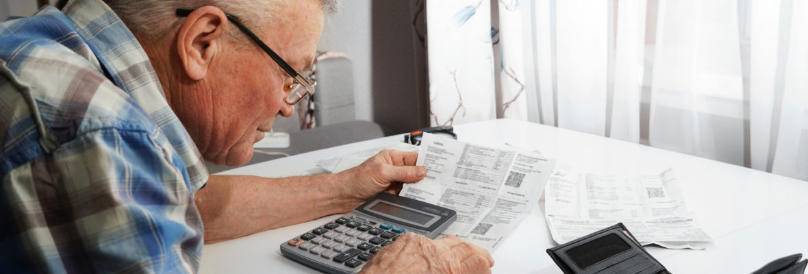 Upset Senior man sitting at the table and calculating finances. Old man checking bills. Man counting coins on the table. Pension calculation concept