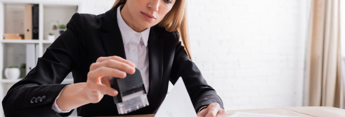 blonde notary holding stamper while working with documents in office.