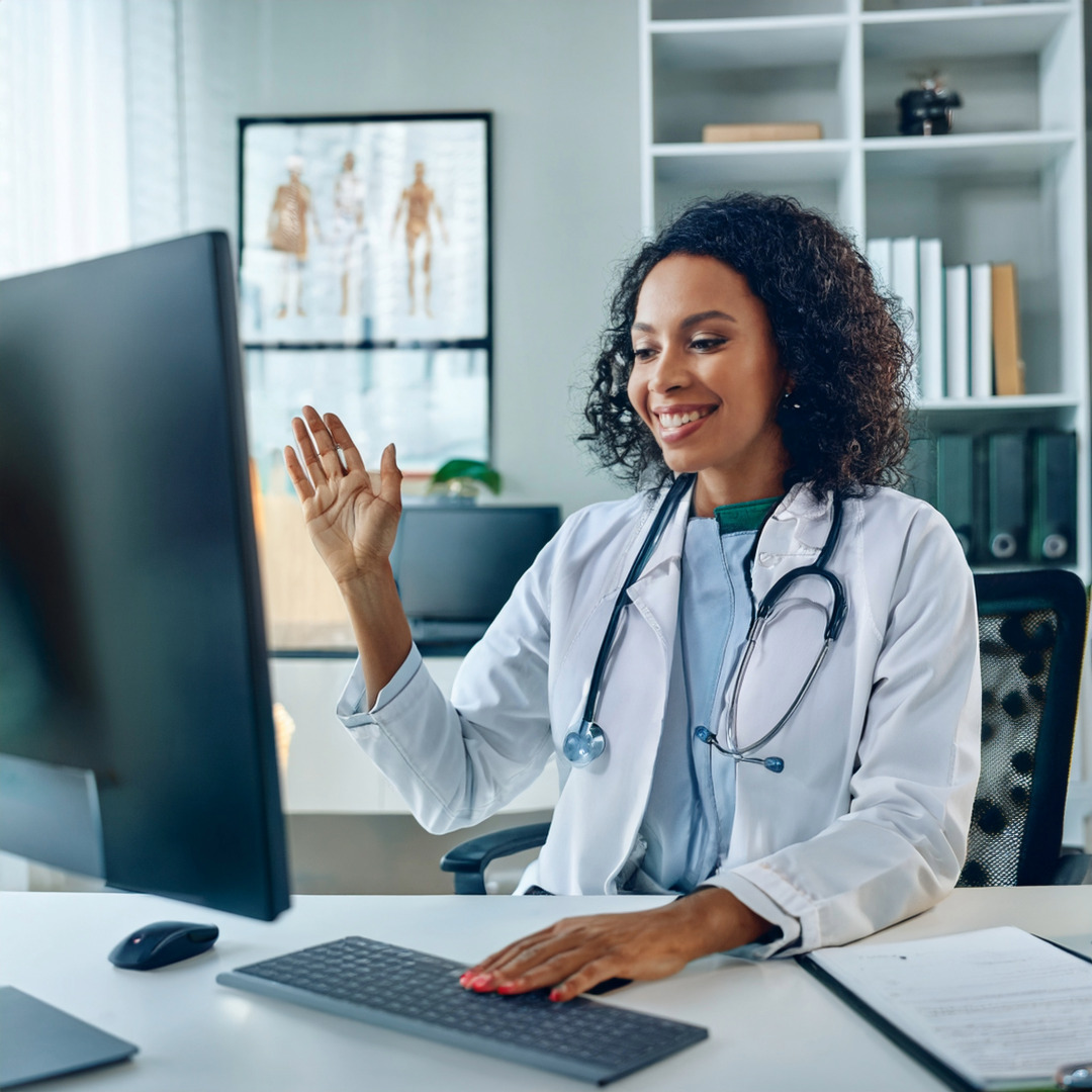 Ärztin sitzt vor einem Computer und macht einen Videochat mit einem Patienten.