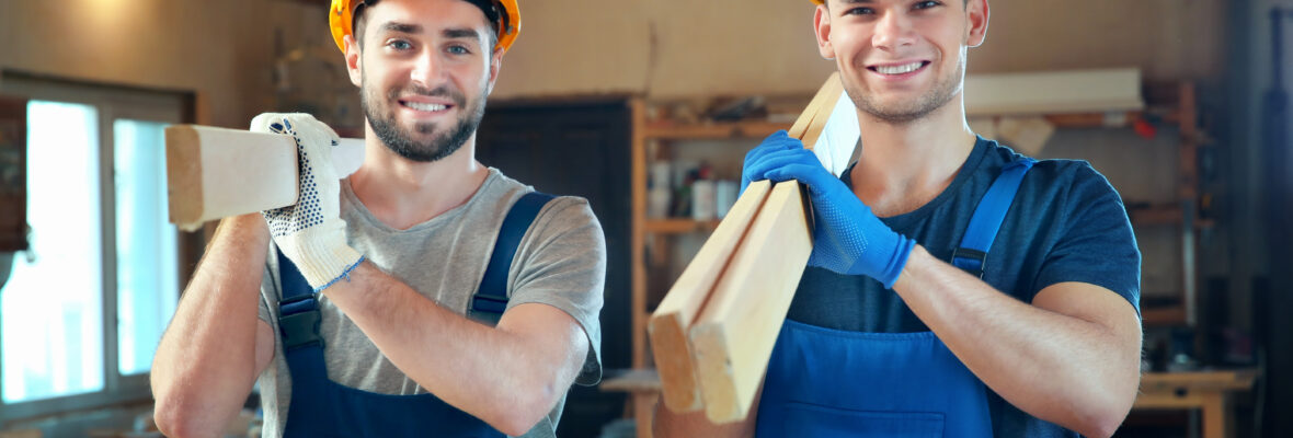 Zwei hübsche junge Tischler mit Brettern in der Werkstatt.