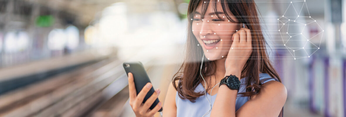 Junge Frau hört Musik mit Kopfhörern von ihrem Handy auf einem Bahnsteig.