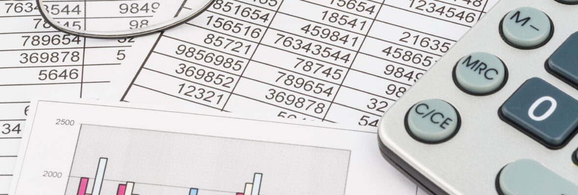 Ein Blick auf einen Arbeitstisch. Darauf liegt eine Tabelle, ein Diagram ein Taschenrechner und eine Brille.