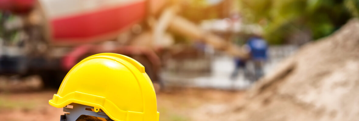 Ein gelber Hartplastikhelm und Bauarbeiterhandschuhe liegen auf dem Drahtgeflecht der Baustelle.